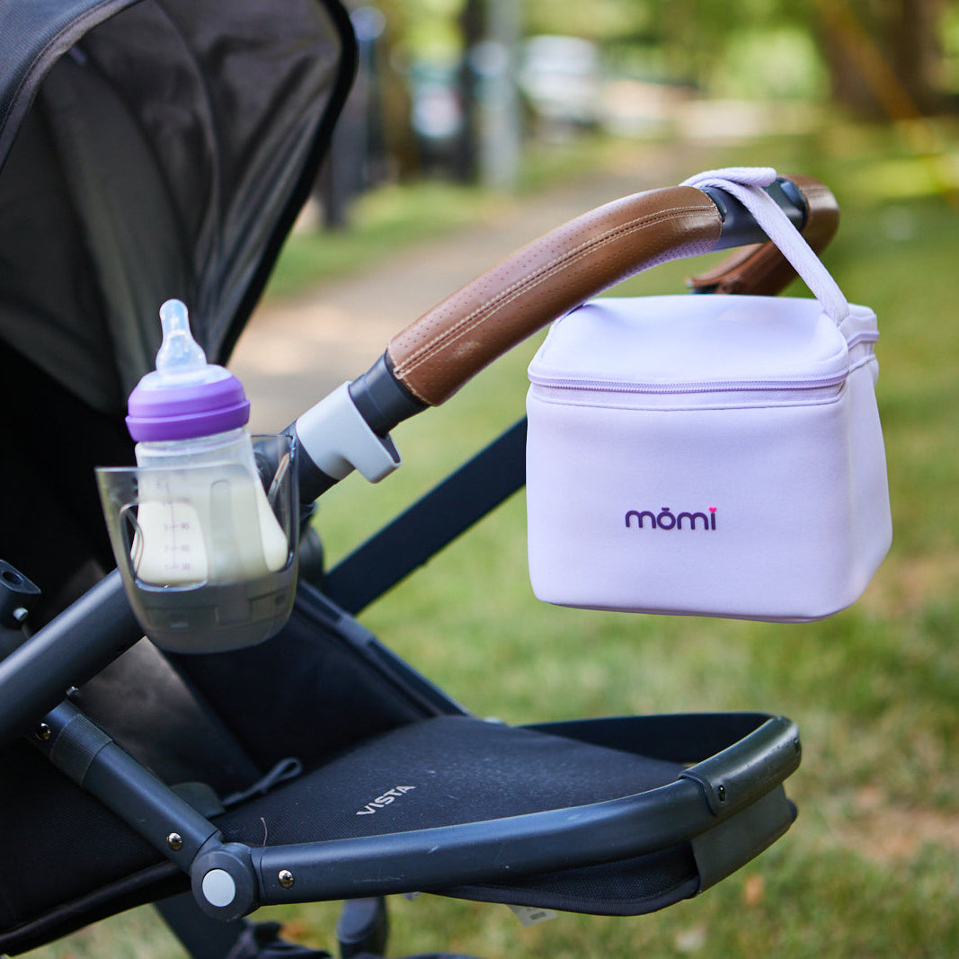 Baby bottle and Momi diaper bag attached to a stroller outdoors.