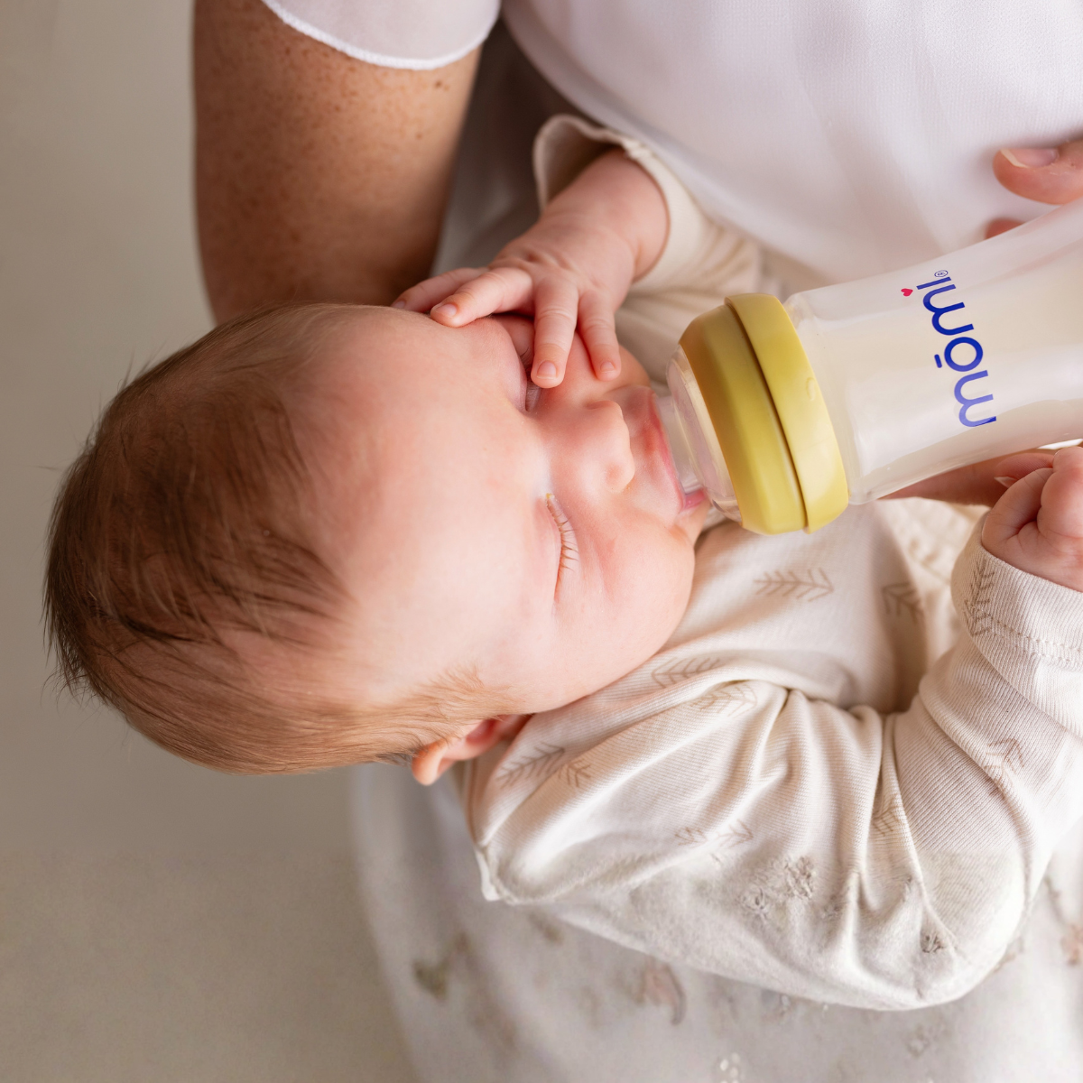 Breastfed baby models a healthy latch being fed from a momi bottle with a honey golden bottle collar